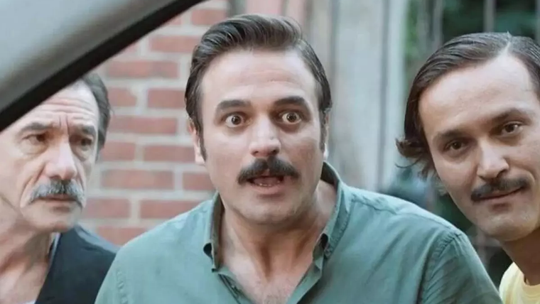 Üç erkeğin bir arada bulunduğu bir sahne, biri şaşkın bir ifadeyle bakıyor.