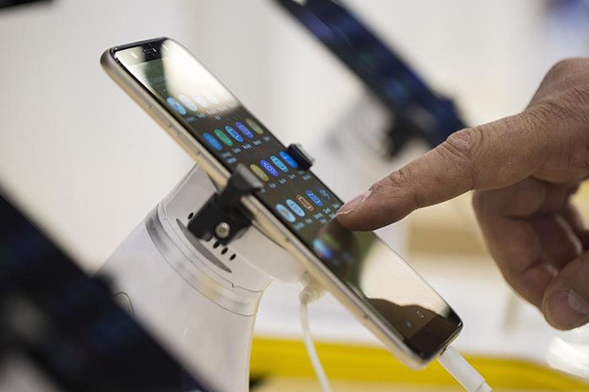 Mağaza standında sergilenen akıllı telefona bir kişinin parmağıyla dokunduğu görülüyor.