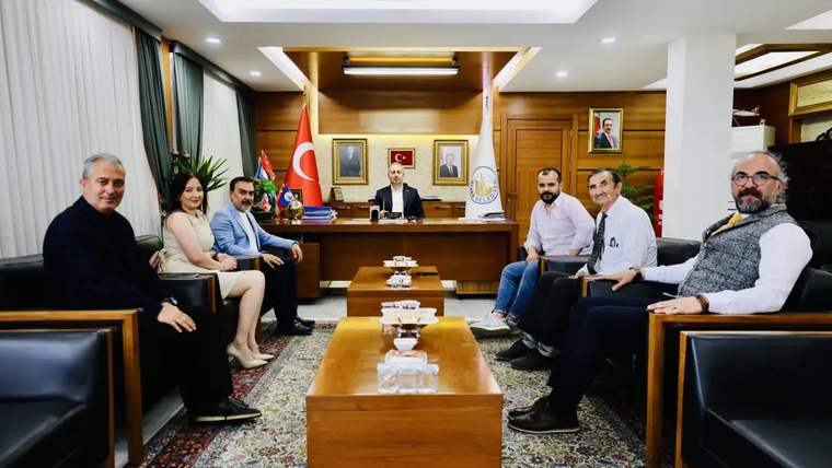 Bir masanın etrafında oturan yedi kişi, arka planda Türk bayrağı ve Sivas Gazeteciler Cemiyeti logosu var.