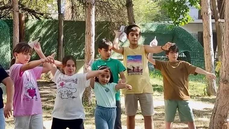 Dış mekanda, çocuklar grup halinde eğlenceli bir etkinlik yapıyorlar.