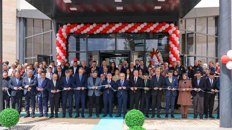 Kırmızı ve beyaz balonlarla süslenen bina girişinde, kurdele ve makas tutan kalabalık yan yana duruyor.