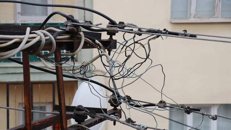 Bina önünde, ahşap direğe bağlı çok sayıda elektrik kablosu ve dağıtım hattı görülüyor.