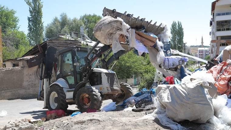 Ön yükleyici iş makinesi, açık alanda çuvallar ve çeşitli atıkların arasında duruyor.