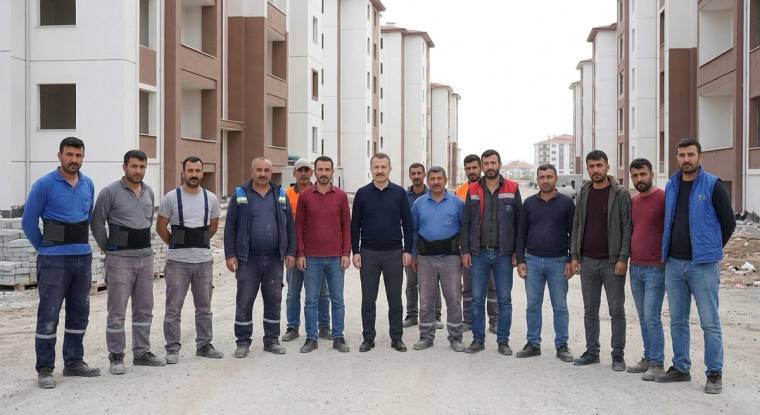 Apartman bloklarının önünde, inşaat alanında yan yana duran bir grup erkek görülüyor.