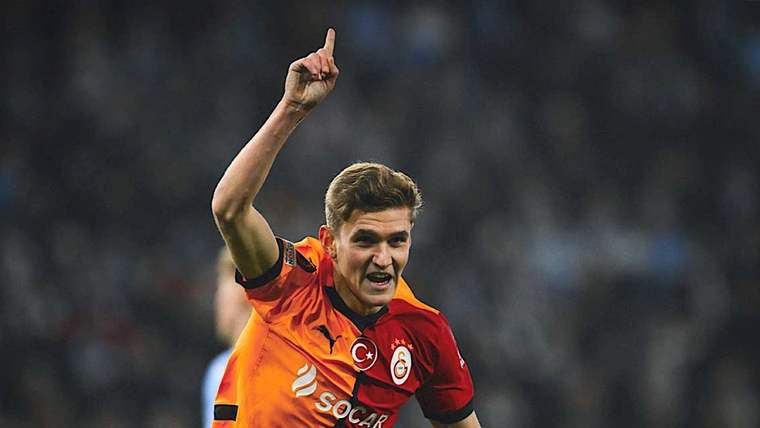 Galatasaray forması giymiş bir futbolcu, gol sevinci yaşıyor ve parmağını yukarı kaldırıyor.
