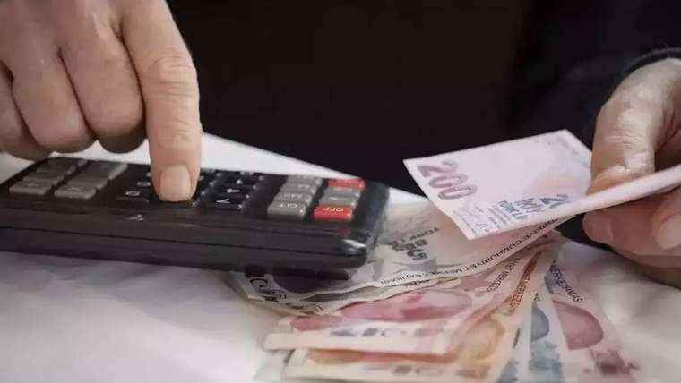 Bir kişinin eli hesap makinesindeki tuşa basarken diğer eli Türk lirası banknotlarını tutuyor.