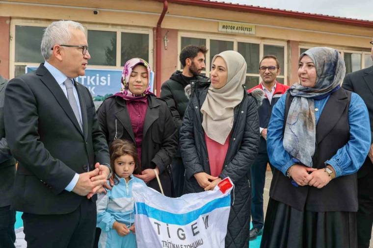 Bir binanın önünde duran yetişkinler ve çocuk, üzerinde "TİGEM" yazılı bir pankartı tutuyor.
