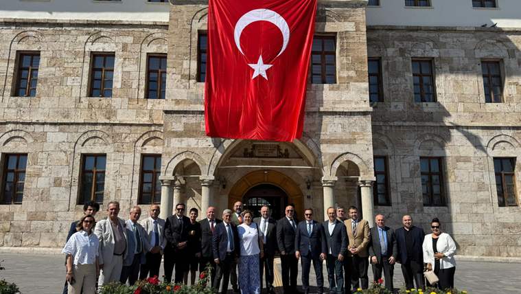 Taş bir binanın önünde, büyük Türk bayrağının altında duran kalabalık bir grup görülüyor.