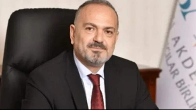 Takım elbiseli ve kırmızı kravatlı bir kişi, makam koltuğunda otururken yanındaki beyaz bayrak kadraja giriyor.