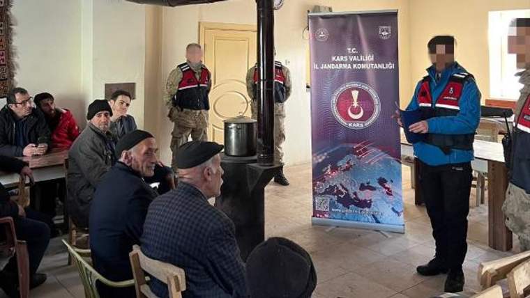 İçeride oturan vatandaşların karşısında jandarma personeli duruyor; arkada Kars Valiliği İl Jandarma Komutanlığı afişi bulunuyor.