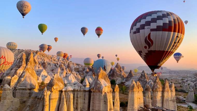 Kayalık peribacalarının üzerinde farklı renklerde çok sayıda sıcak hava balonu gökyüzünde süzülüyor.