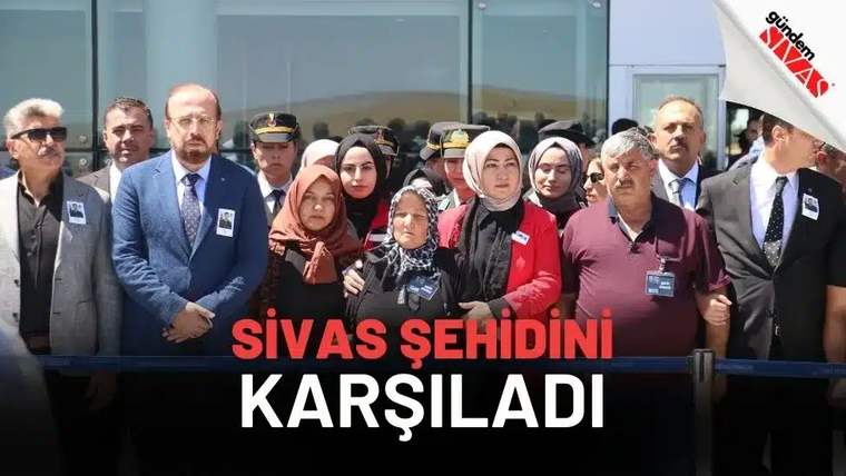 Bir bina girişinde, aralarında üniformalı görevlilerin de bulunduğu kalabalık bir grup yan yana duruyor.