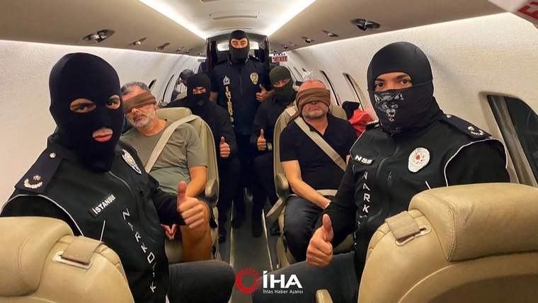 Uçak kabininde yüzleri maskeli dört görevli, yanlarındaki iki sivil erkekle birlikte başparmaklarını kaldırıyor.