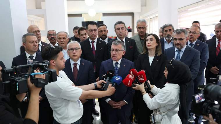 Bir grup insan, basın toplantısında mikrofonlara yanıt veriyor. Arkada kalabalık bir izleyici var.