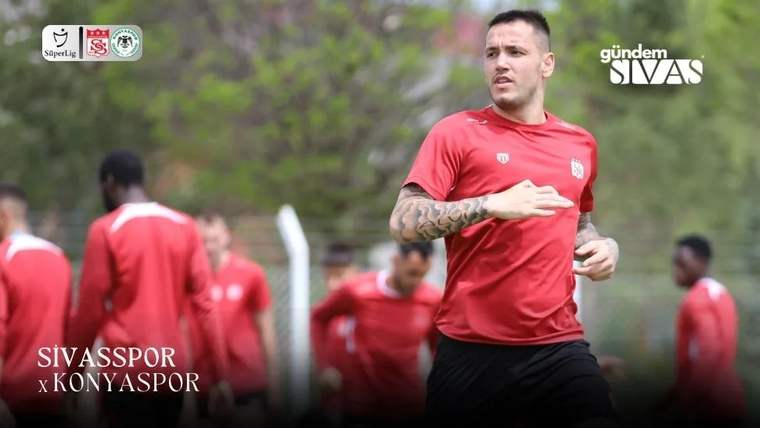 Kırmızı formalı bir futbolcu koşarken görülüyor; arka planda aynı renk formalar giyen oyuncular bulunuyor.