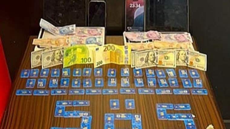 Bir masa üzerinde farklı para birimlerine ait banknotlar, çok sayıda mavi kart ve iki cep telefonu bulunuyor.