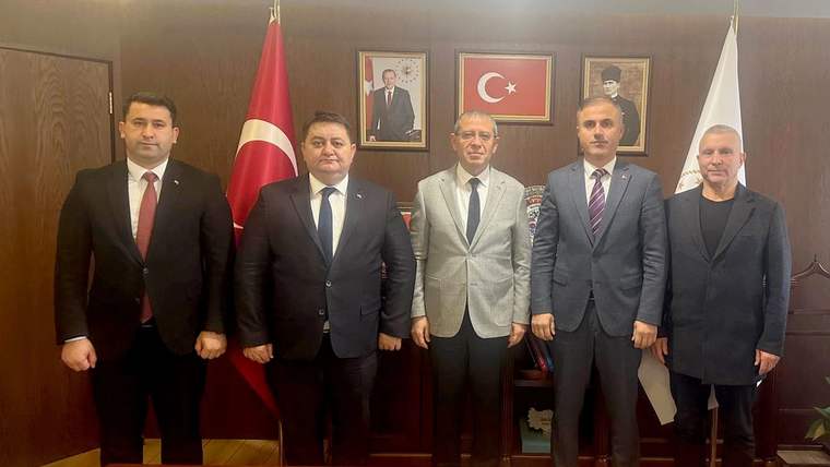 Ahşap panelli bir ofiste, Türk bayrakları ve portreler önünde takım elbiseli beş kişi yan yana duruyor.