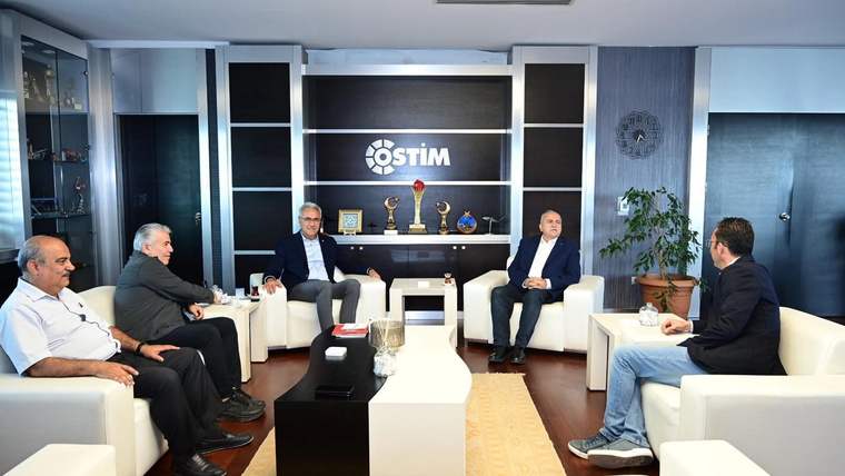 Bir grup erkek, modern bir ofis ortamında toplantı yapıyor. Arka planda ödüller ve bitki var.