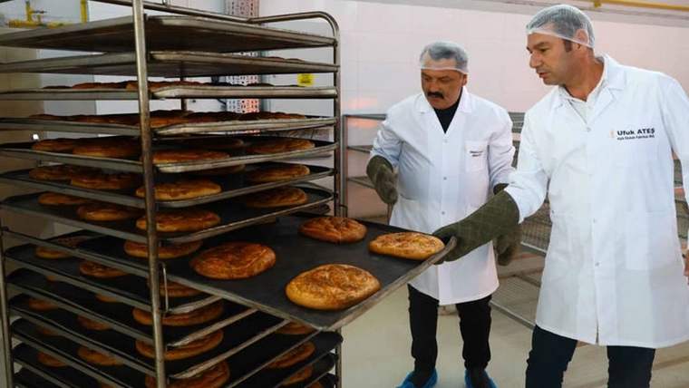 Fırın tepsisiyle ramazan pidesi çıkaran iki kişi, beyaz önlük ve bone giymiş.