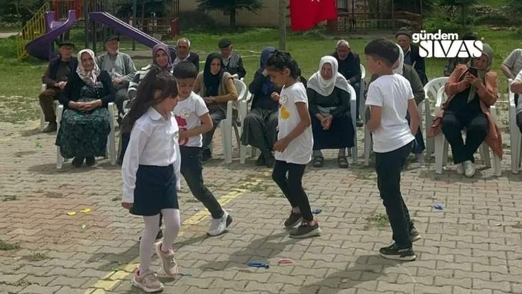 Dört öğrenci, açık alanda dans ederek 23 Nisan'ı kutluyor, arka planda izleyiciler var.