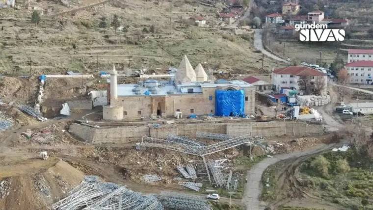 Yamaçta minareli bir yapı, mavi örtüyle kapatılmış bölümleri ve çevresindeki inşaat alanıyla görülüyor.