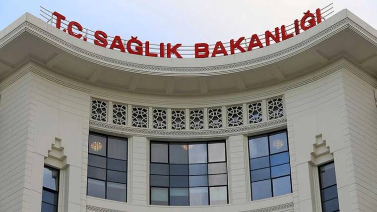 Üst bölümünde kırmızı harflerle “T.C. SAĞLIK BAKANLIĞI” yazan beyaz bir kamu binası görülüyor.