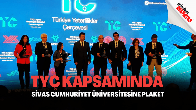 Plaket alan kişiler, arka planda TYÇ logosu ile birlikte sahnede duruyor.