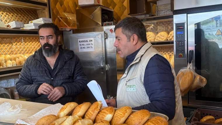 Ekmeklerle dolu tezgâhın arkasında iki erkek, fırının içinde yan yana duruyor.