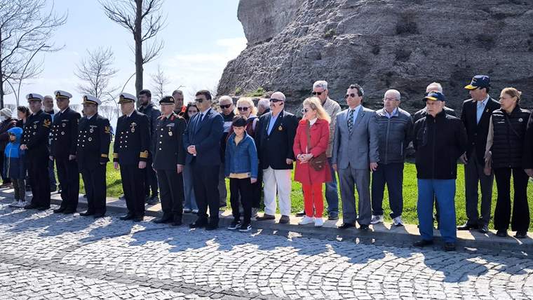 Üniformalı görevliler ve sivil kişiler, kayalık bir alanın önünde yan yana duruyor.