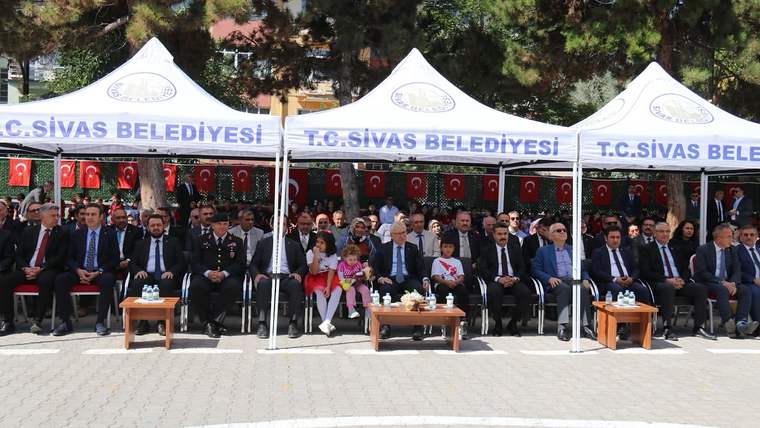 “T.C. Sivas Belediyesi” yazılı çadırların önünde, Türk bayrakları arasında oturan yetişkinler ve çocuklar görülüyor.