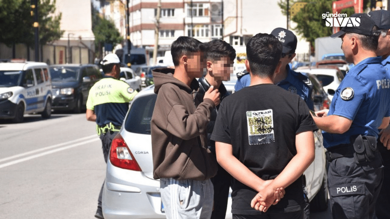 Polis memurları, bir grup genci araçların yanında denetliyor.