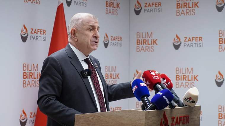 Zafer Partisi logosunun arkasında, mikrofonların önünde konuşan bir kişi.