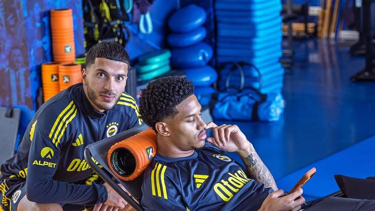 Fenerbahçe forması giymiş iki futbolcu, birinin arkasında durarak diğerinin telefonuna baktığı bir an.