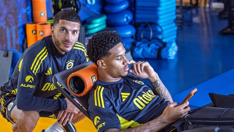 Fenerbahçe forması giymiş iki futbolcu, birinin arkasında durarak diğerinin telefonuna baktığı bir an.