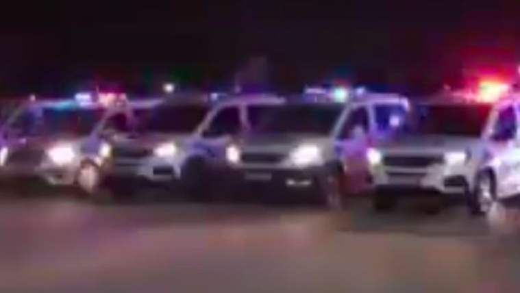 Aydınlatma lambaları yanmış, arka planda polis araçları sıralanmış.