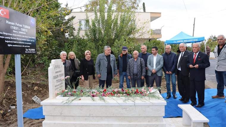 Bir grup insan, Hasan Fehmi öğretmenin mezarının başında duruyor, mezar çiçeklerle süslenmiş.