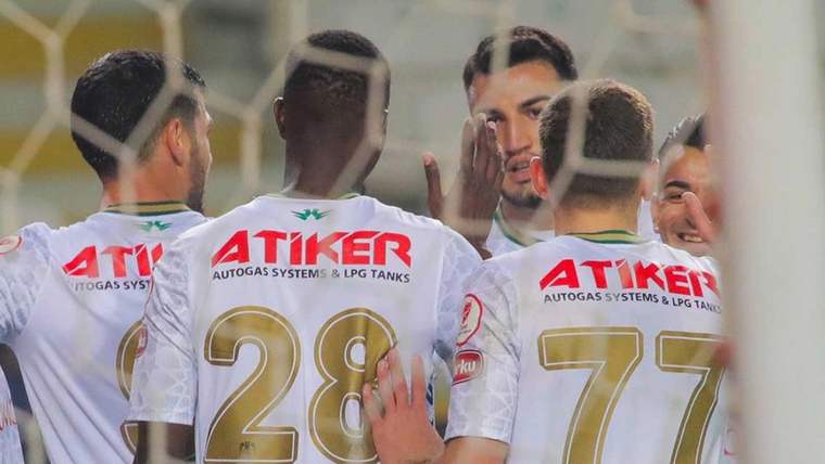 Atiker yazılı formalar giymiş futbolcular, birbirlerine sevinçle sarılıyorlar.