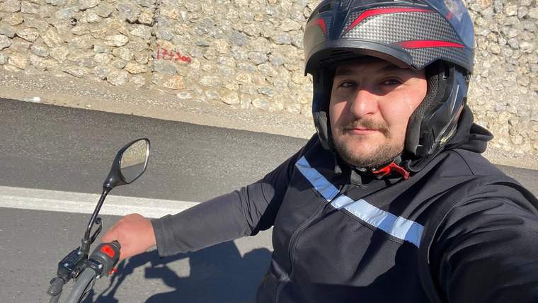 Yolda motosiklet süren bir kişi, kask takmış ve selfie çekiyor.
