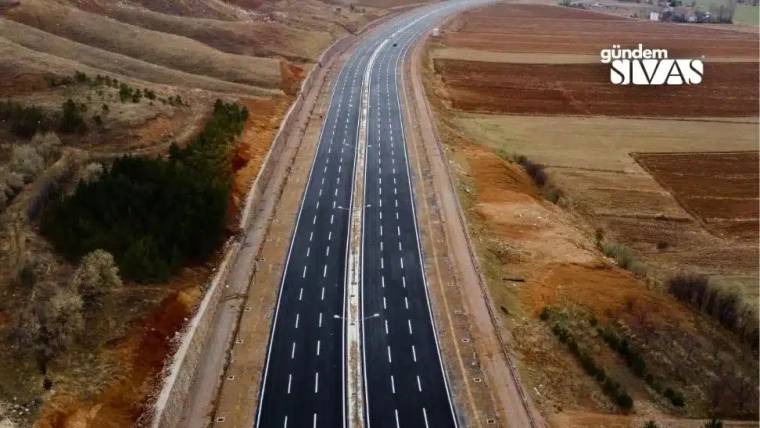 Geniş bir bağlantı yolu, tarım arazileri arasında uzanıyor ve her iki yönü de açık.