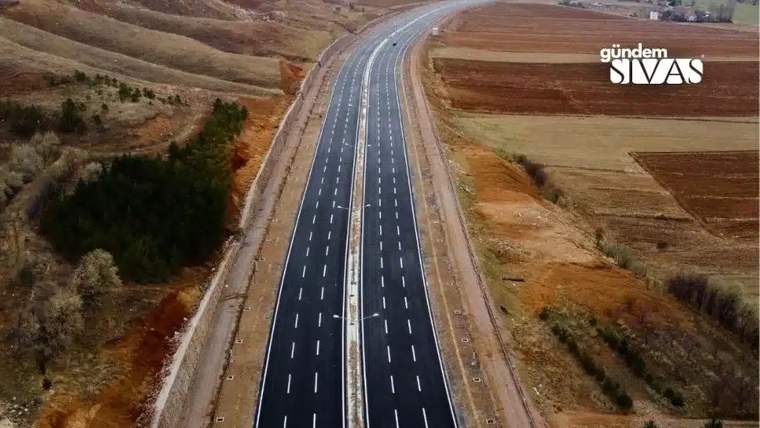 Geniş bir bağlantı yolu, tarım arazileri arasında uzanıyor ve her iki yönü de açık.