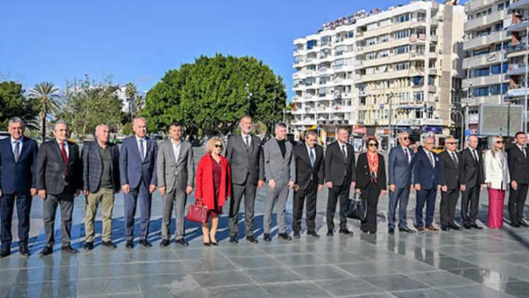 Açık alanda, aralarında kırmızı montlu bir kadının da bulunduğu bir grup insan yan yana duruyor.