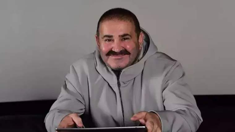 Gri bir mont giymiş, gülümseyen bir adam, tablet bilgisayara bakıyor.