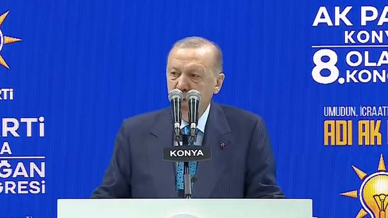 Mikrofonun önünde konuşan bir kişi, arka planda mavi bir pano var.