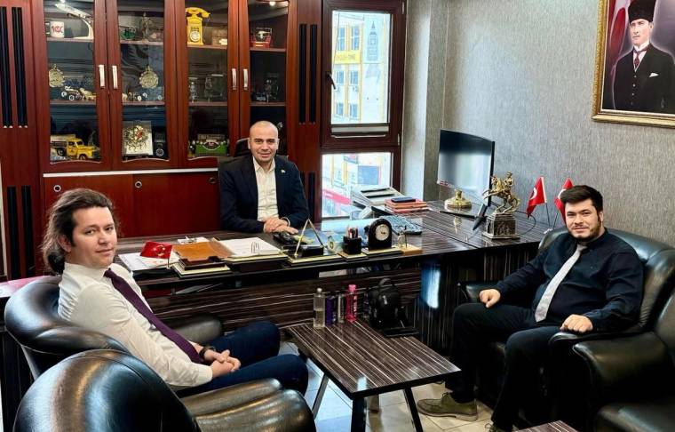Bir masanın etrafında oturan üç kişi, arka planda Türk bayrağı ve Atatürk portresi var.