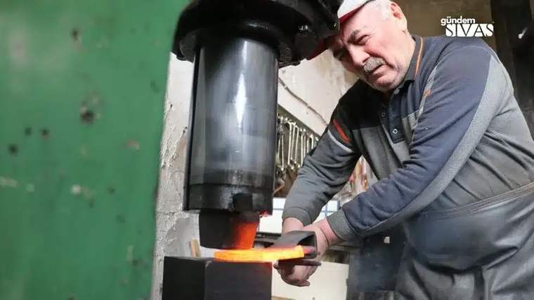 Demir dövme makinesiyle çalışan bir usta, sıcak demiri şekillendiriyor.