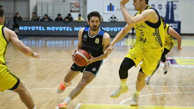 Basketbol sahasında siyah formalı oyuncu top sürerken sarı formalı rakibi savunma yapıyor.
