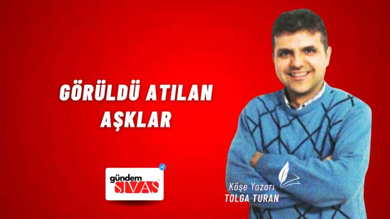 Kırmızı arka planda, mavi kazak giymiş bir kişi gülümseyerek poz veriyor.