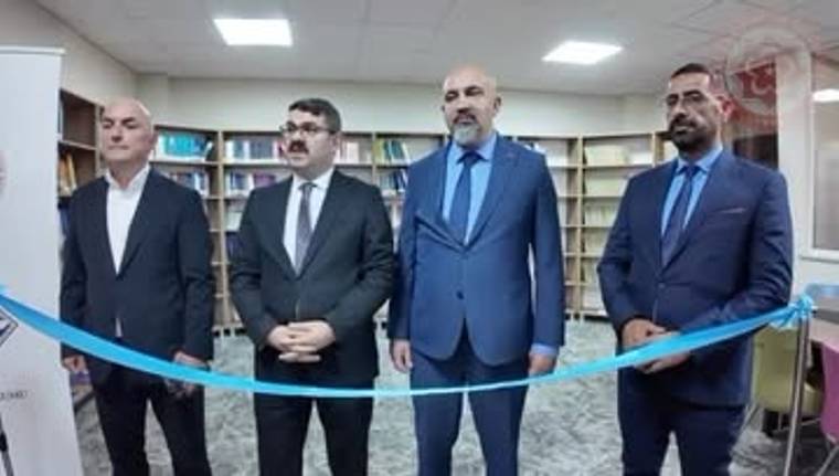 Kitaplık rafları önünde duran dört kişi, mavi kurdeleyle ayrılmış alanın arkasında görülüyor.