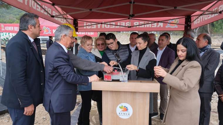 Bir grup kişi, üzerinde Kemer Belediyesi logosu bulunan kürsü önünde kurdele kesme töreni yapıyor.