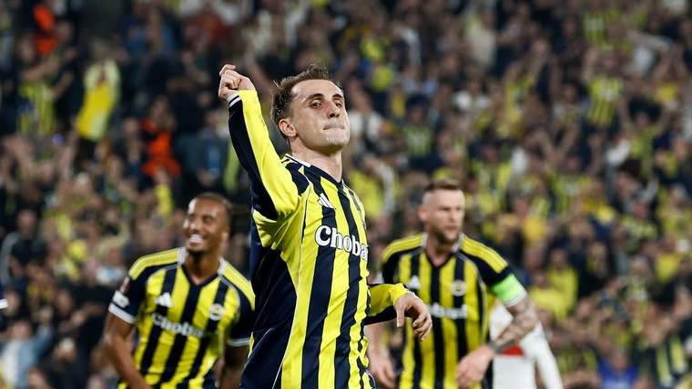 Sarı lacivert çubuklu formalı bir futbolcu sahada kolunu kaldırırken, takım arkadaşları ve tribünler görülüyor.